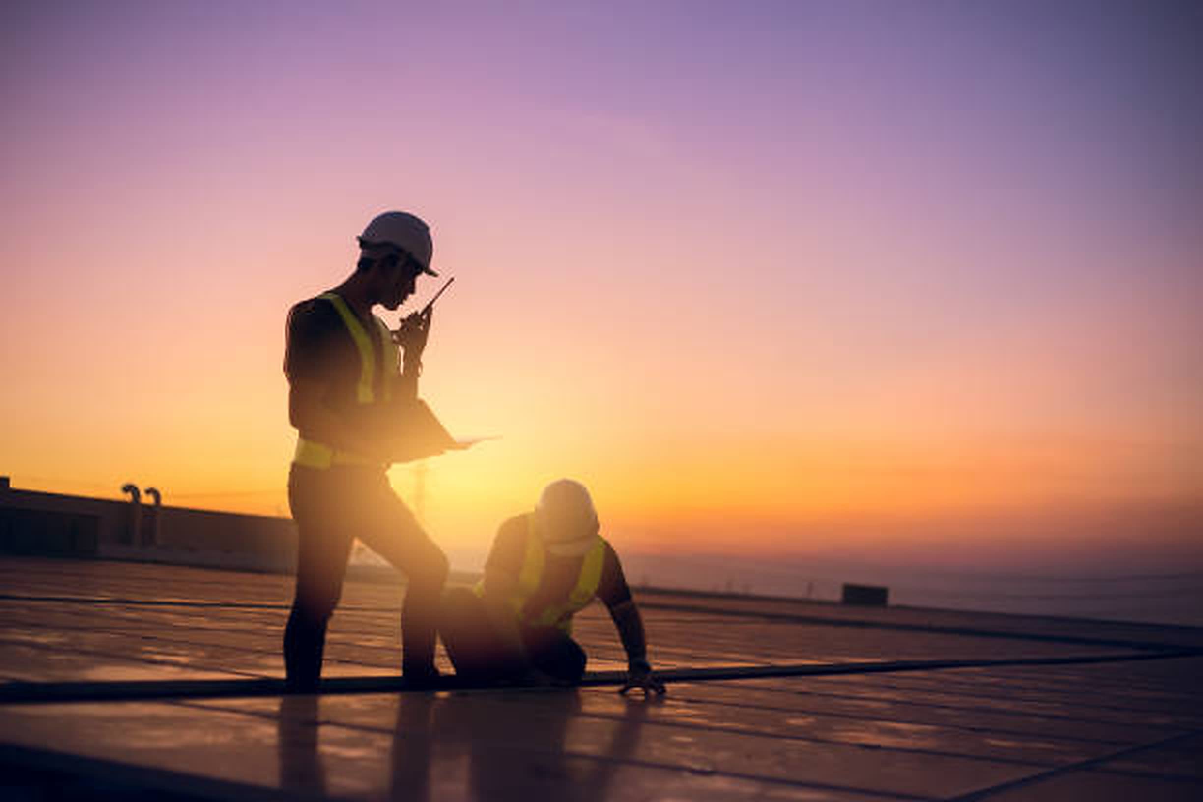 Technicians in hard hats servicing equipment on a rooftop at sunrise