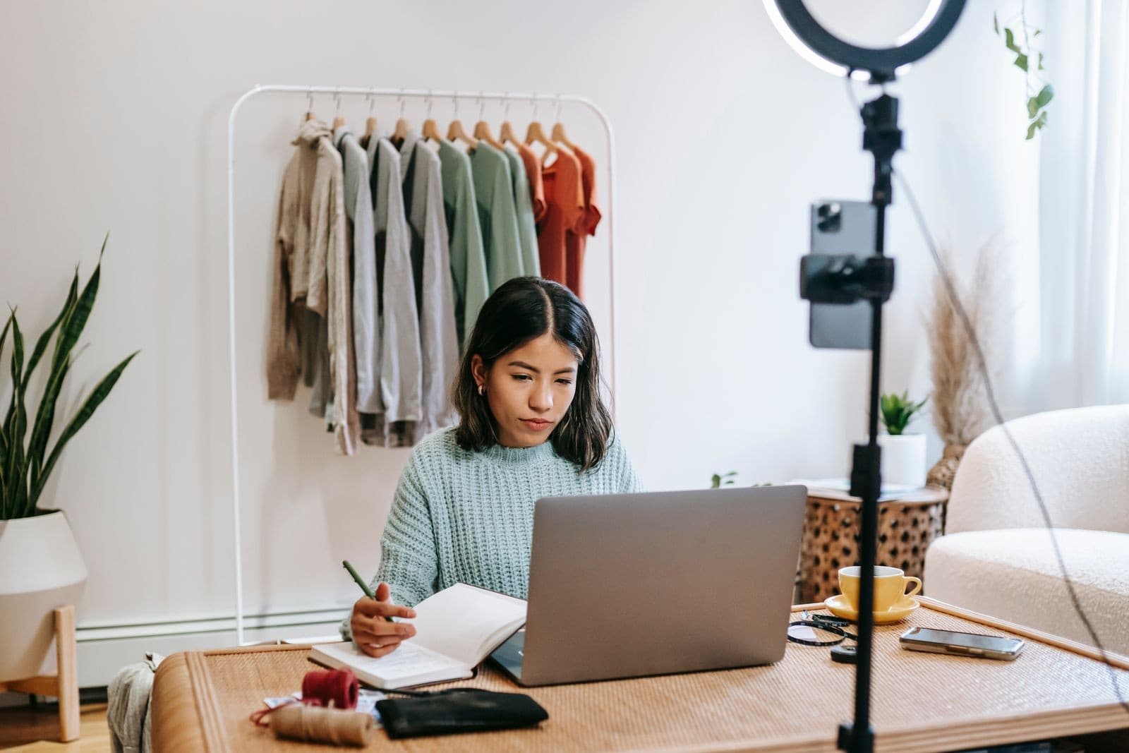Boutique owner managing online orders at her laptop beside a clothing rack